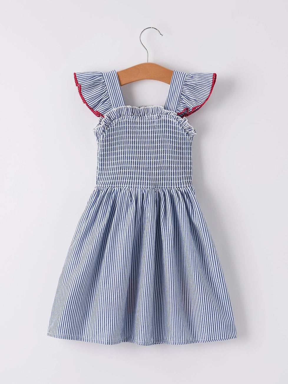 A blue and white striped sleeveless toddler dress with ruffled cap sleeves and red piping, hanging on a wooden hanger against a light gray background.