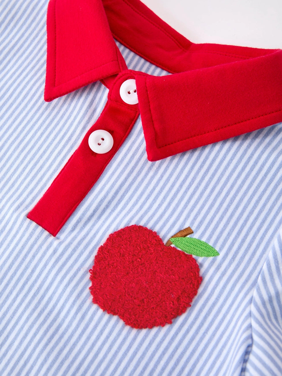 Red collar with buttons and a red apple patch on a blue striped background